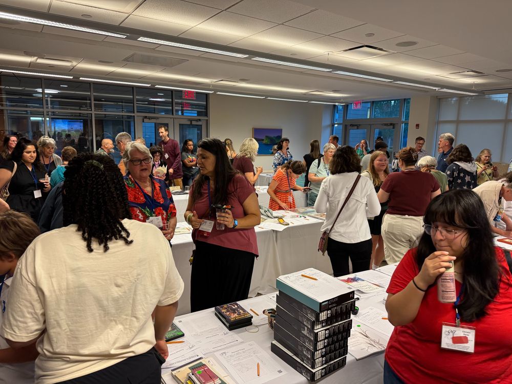 A photo showing members of the GNSI mingling and chatting around multiple white tables displaying various items from the 2025 silent auction
