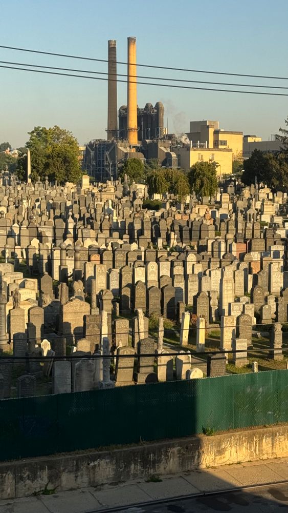 a view of endless graves and tombstones crowded on a hill with a belching factory smokestack in the background 