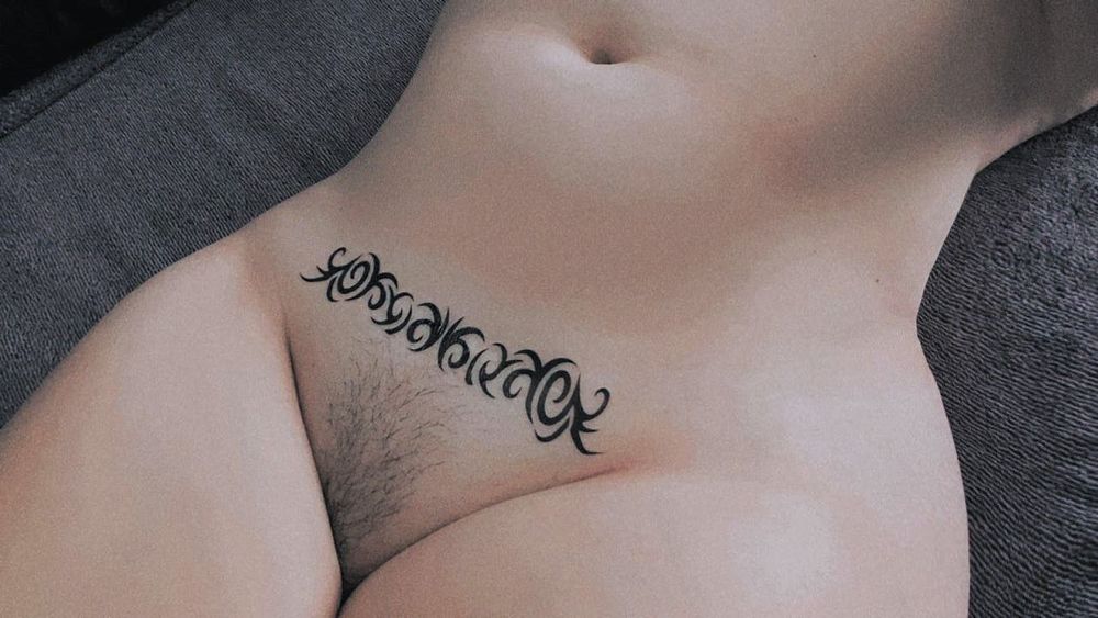 Poppy Carmine in 2025 laying naked on a purple blanket showing their tummy & pubic hair.