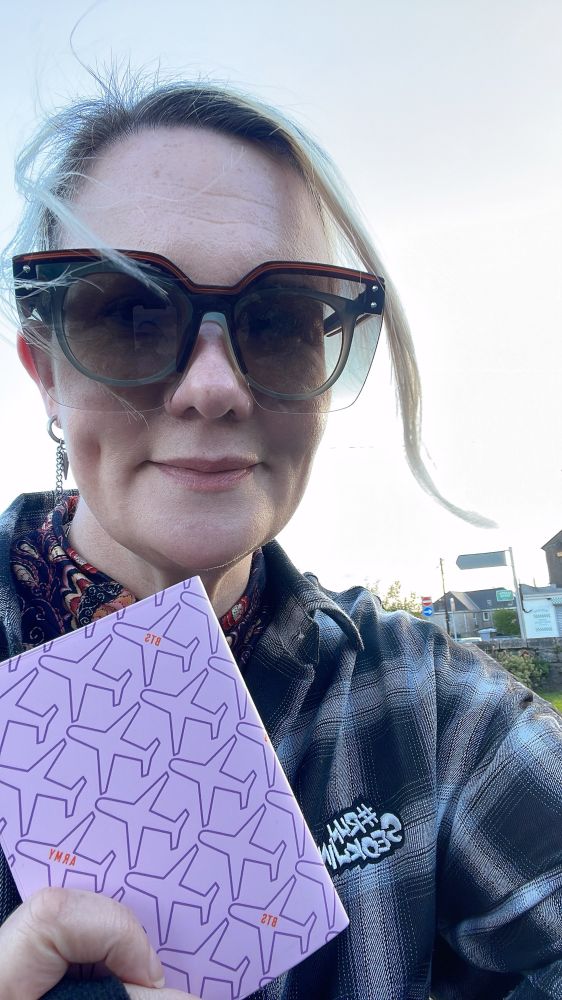 A photo of me wearing sunglasses (and glasses under them) showing the cover of my passport- which is covered with purple airplanes. 