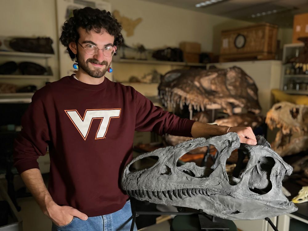 Finishing undergrad Peter Rhynard in his new Virginia Tech sweatshirt poses next to Big Al the Allosaurus (MOR 693), the focus of his honors thesis research.