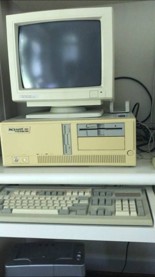 Older horizontal beige and white computer with a monitor on top and keyboard on a deks's slide out tray underneath.