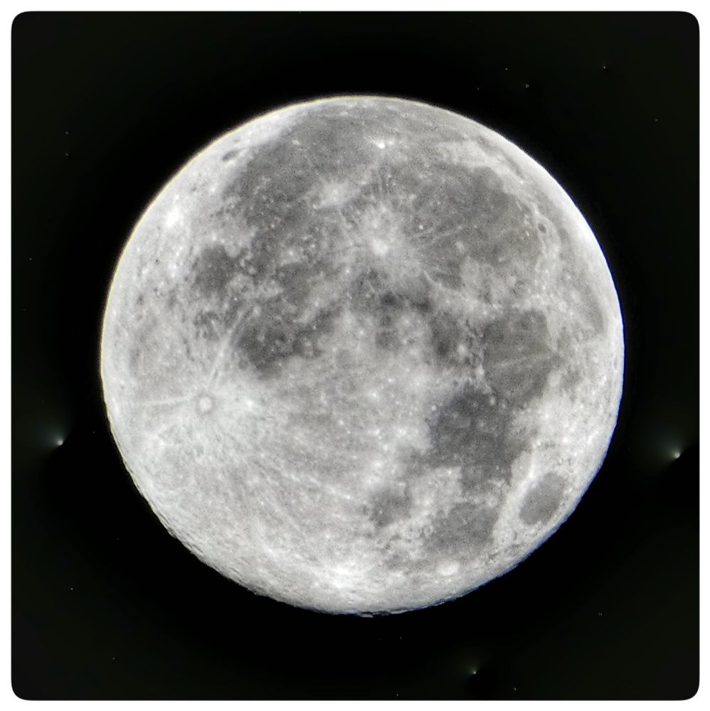 The image depicts a detailed view of the November 5, 2024 supermoon (also known as Beaver Moon) against a black background. The supermoon is the primary subject, dominating the center of the frame. Its surface is textured with numerous craters, ridges, and dark patches, giving it a rough, three-dimensional appearance. The colors are primarily shades of gray and white, with the darker areas representing the lunar "seas" or lowlands and the lighter areas highlighting the highlands and impact craters.

The background is a deep black, punctuated by small, bright stars. These stars are scattered randomly, adding depth and a sense of vastness to the scene. The image is framed within a white border, which creates a sense of separation and focus. The overall composition is symmetrical, with the full moon centered, drawing the viewer's eye directly to its detailed surface. The image evokes a sense of wonder and the mystery of space.