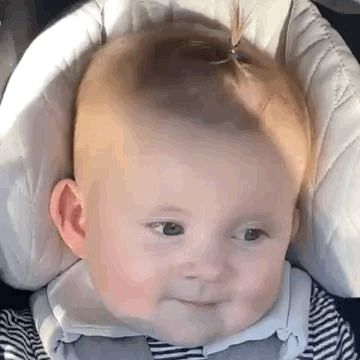 a baby is sitting in a car seat and making a funny face .