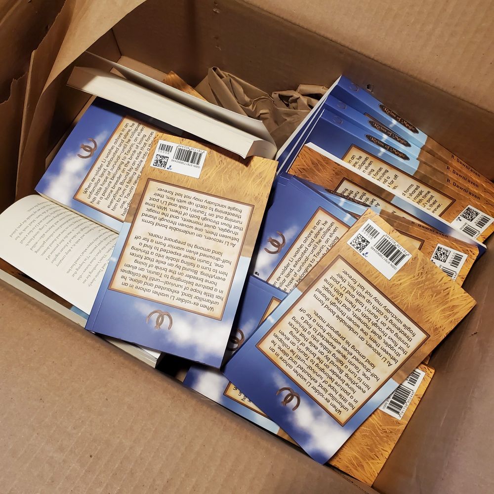 Photo showing paperback copies of Reins of Magic loosely packed in a box that is too large , so they are in complete disarray. Inner pages of one book are exposed.