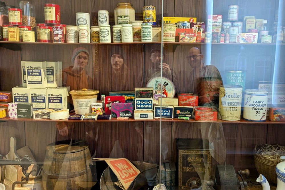 A photo of 4 people taken in the reflection of a glass case in the McManus museum containing many vintage food packing examples