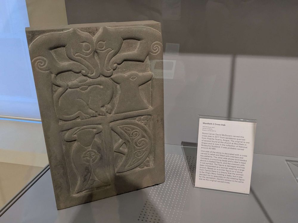 A cool old stone slab, it's info card reads: "Monifieth 2 Cross-Slab. David McGovern. Carved Sandstone. One side of the stone is decorated with a cross carved in relief and filled with interlace and key patterns. The other side shows bird-headed monsters, a crouching beast and a deer's head above a cloaked figure, and the crescent with V-rod symbol. The figure is damaged and has been interpreted as a woman wearing a large brooch. Based on a similar figure on a stone from Canna there is a theory that the woman is the Virgin Mary holding a baby, but it was decided not to speculate on the missing figure for the recreation."