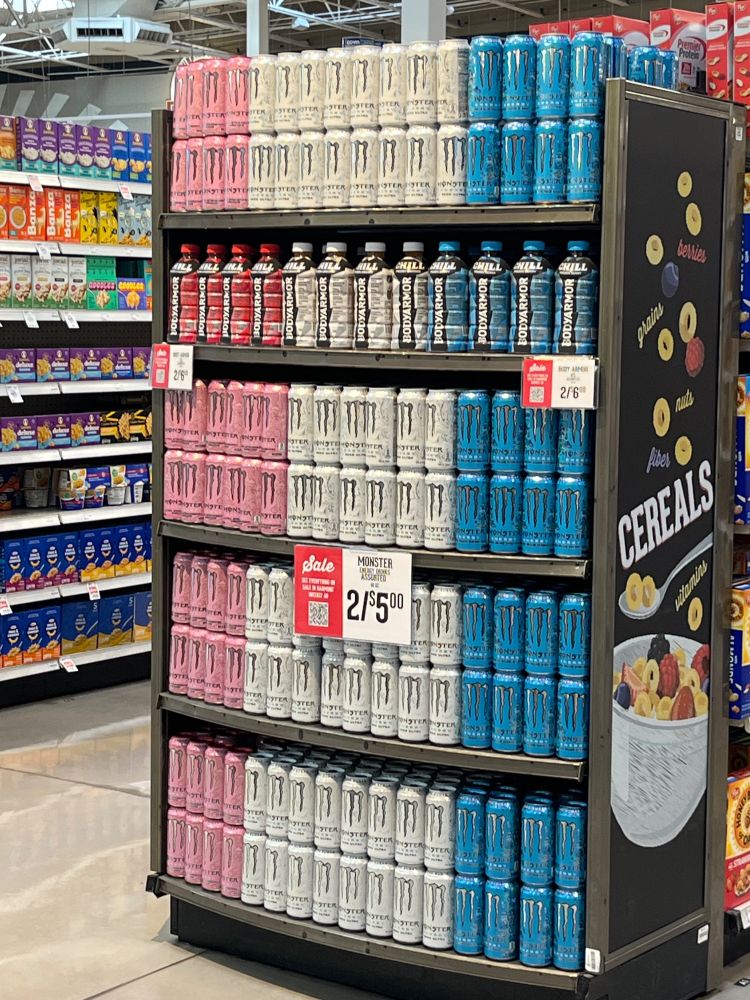grocery store end cap display of light pink, white, and light blue cans of monster, the colors of the transgender flag