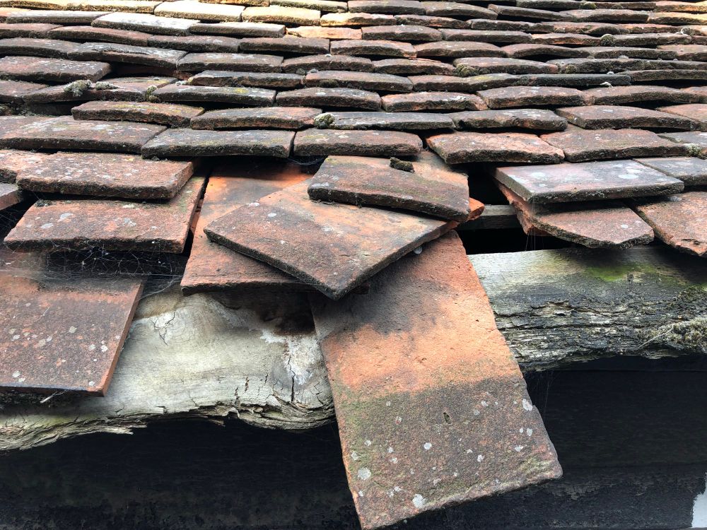 Red and grey with flecks of white, clay roof tiles, but a couple are dislodged in the centre showing the wood beam underneath.