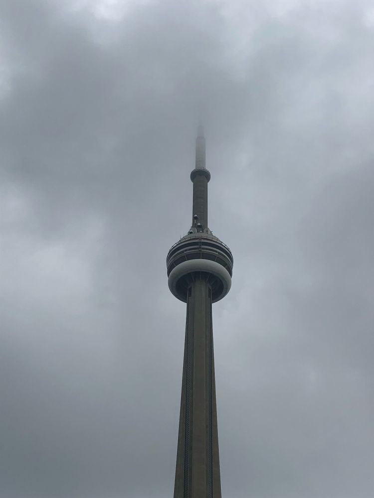 The CN Tower in Toronto, Canada, shrouded in grey clouds and mist.