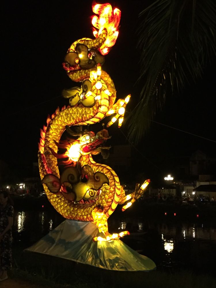 A lighted dragon sculpture at night by the water