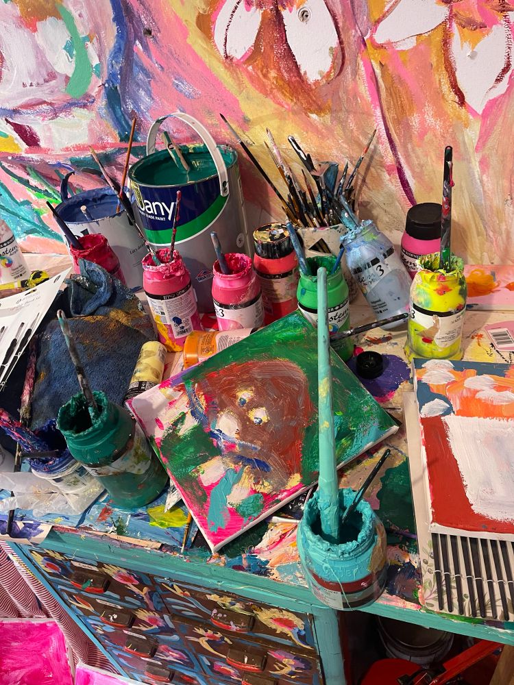 Small painting of a mole canvas on a busy worktop covered in bright paint pots 