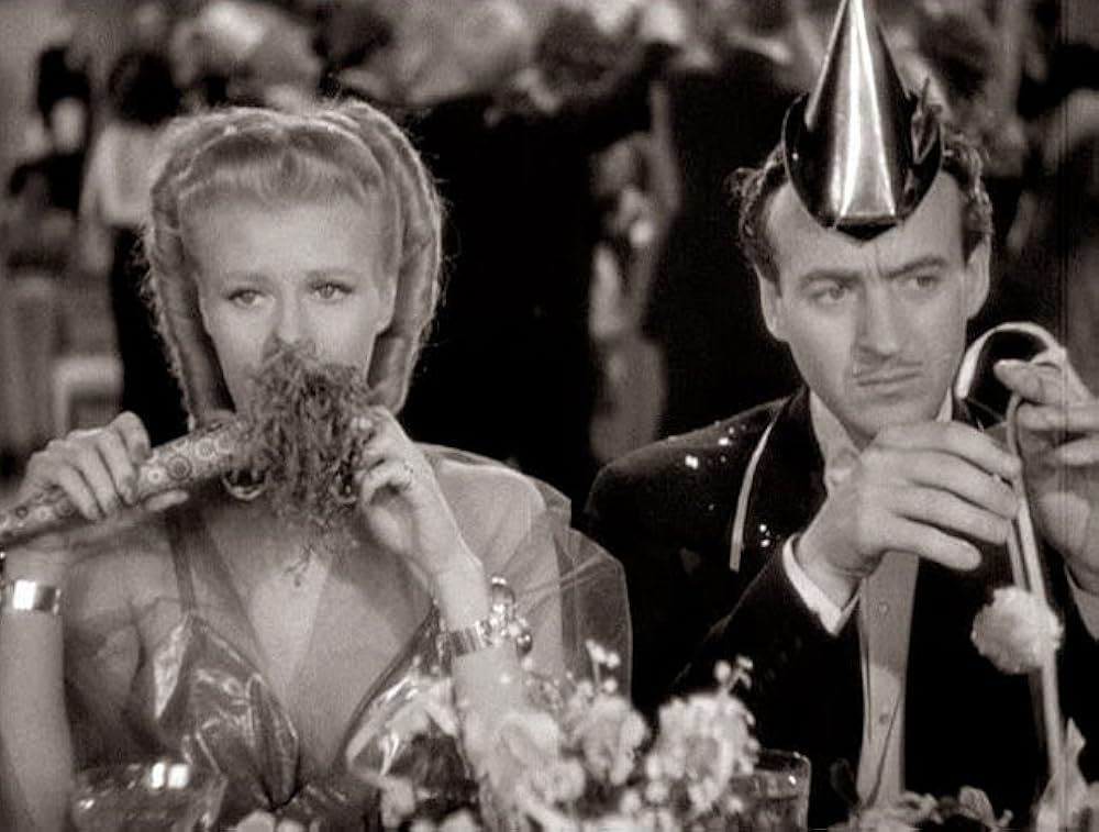 A still from the movie Bachelor Mother, with Ginger Rogers and David Niven. Their two characters are dressed in formalwear, with Niven in a party hat. 