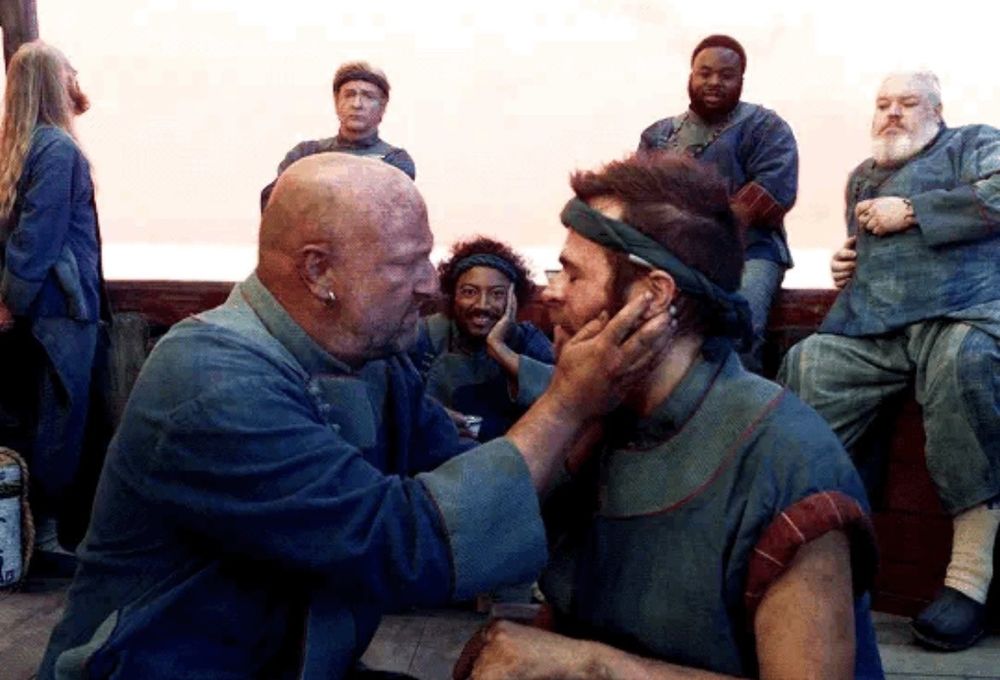 Black Pete and Lucius reuniting. Pete holds Lucius' face in his hands. Roach is in the background, framed between their faces. He is very much enjoying watching their reunion. Buttons, Stede, Oluwande, and Wee John are also in the background leaning against the ship rail.