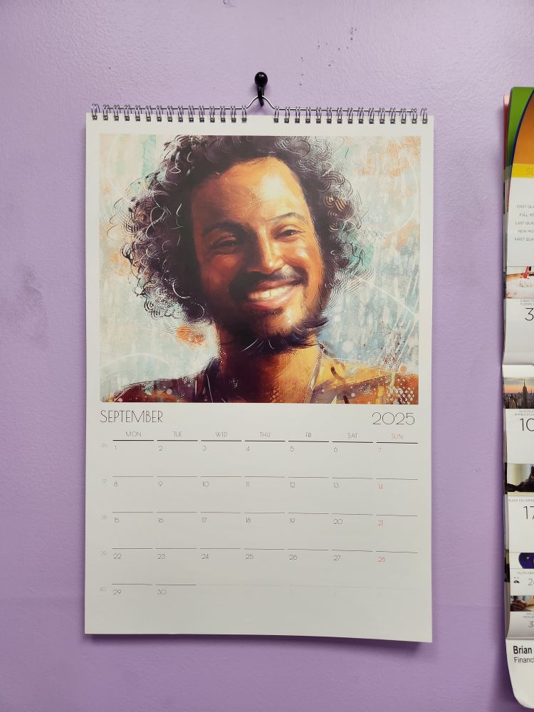 A calendar hangs on a purple wall. It is turned to the month of September. It shows a beautiful portrait of Roach smiling.