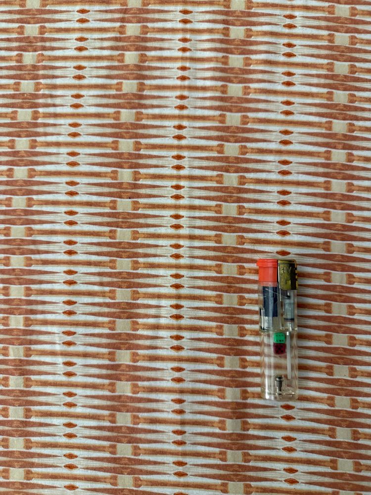 I rather unusual lighter as far as American standards go like BIC and cricket lighters. Clear with one black and one green die inside. The lighter is on top of fabric that is orange tiki type fabric with triangles and squares.