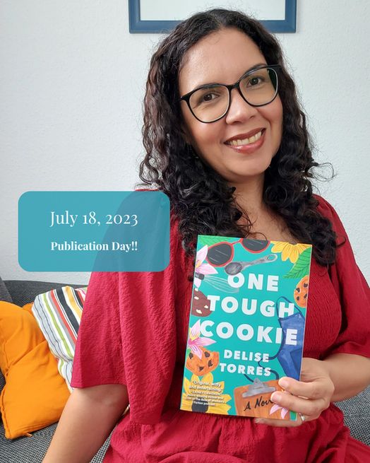 Delise Torres smiling proudly, holding her debut novel 'One Tough Cookie' on publication day, July 18, 2023.