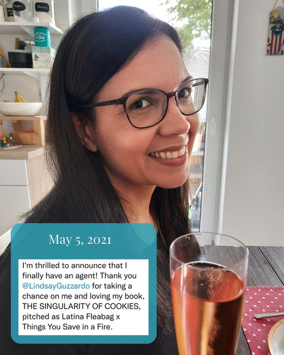 Delise Torres, with long dark hair and glasses, smiles while holding a glass of sparkling wine; a text box displays an announcement that she finally signed with a literary agent.