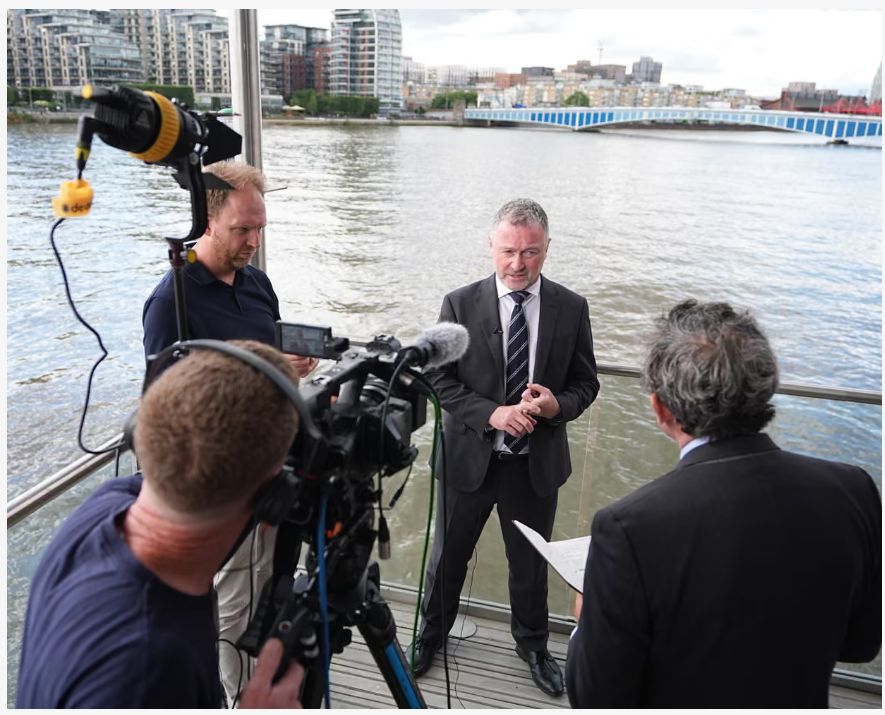 Photo of Environment Secretary Steve Reed speaking to the media at Kingfisher Wharf, London, today, after announcing the abolition of Ofwat. A film crew with interviewer, boom mic and camera, are pictured facing away from the viewer.
