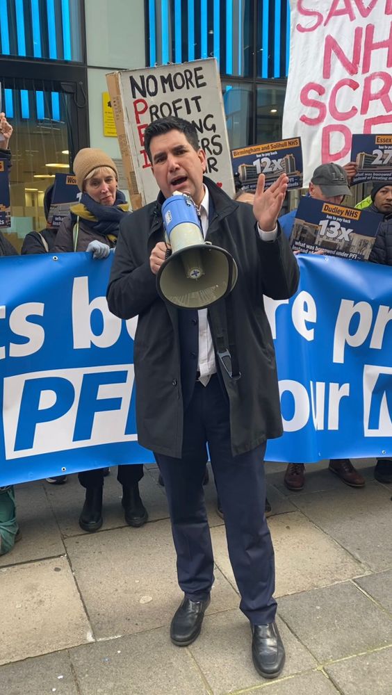 Richard Burgon MP holding a megaphone in front of a line of protesters holding a large blue banner.