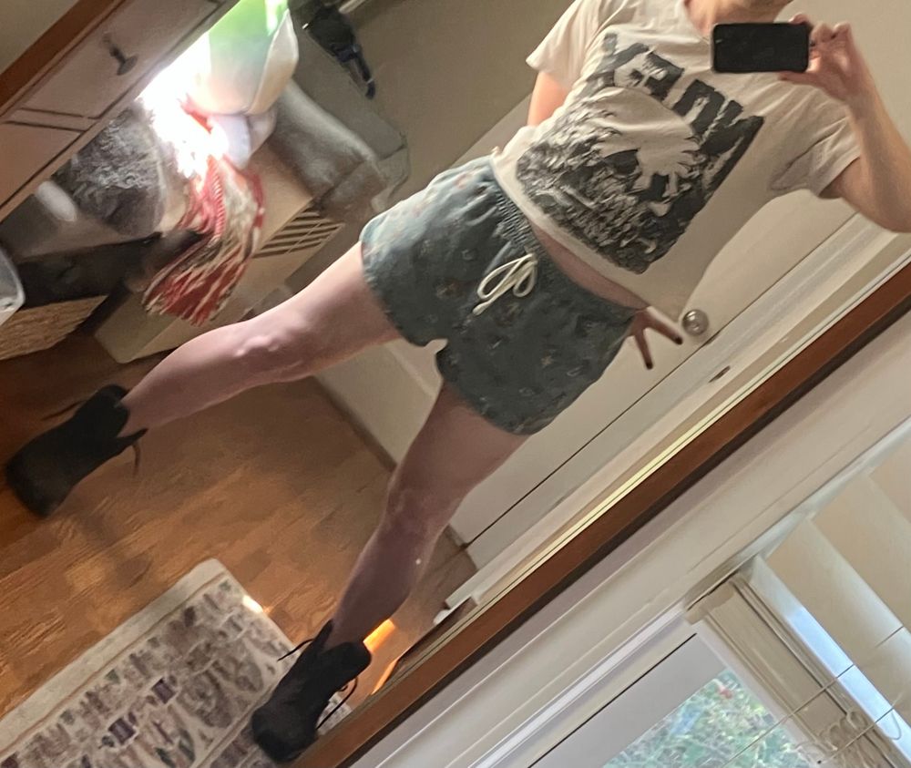 cute enby black nail polish black boots
cropped off-white nofx t-shirt with skull
sm inseam blue mushroom shorts with tie

wide stance with a bit of tummy showing and a subtle peace sign behind the back

bedroom mirror, wood floors, rug, bench with blankets, natural light