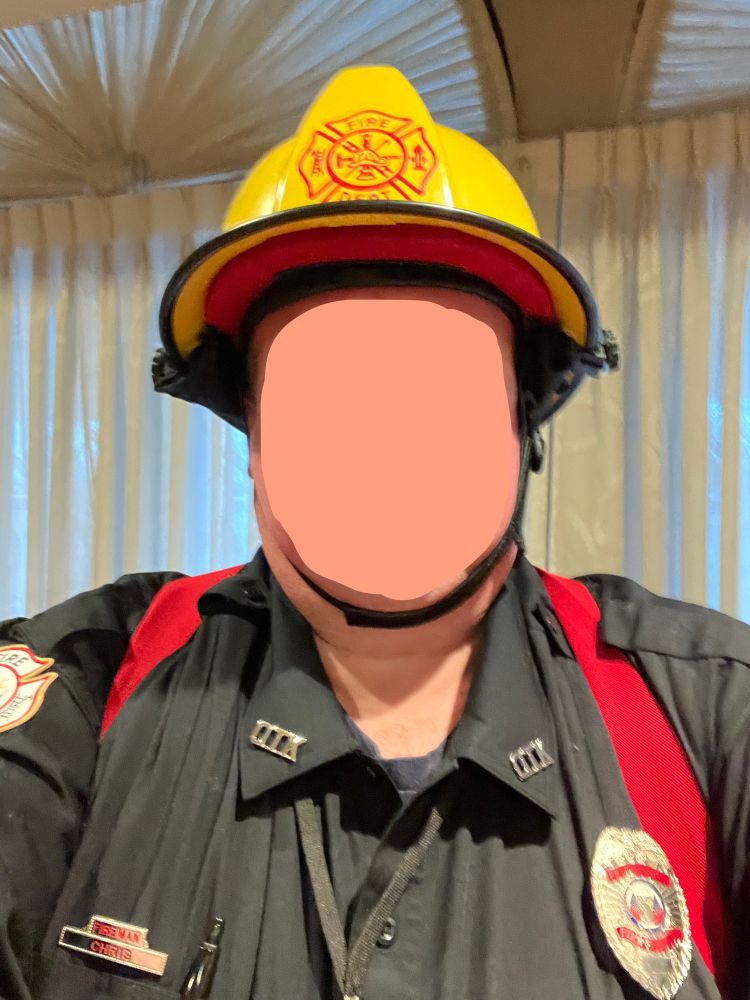 A photo of my firefighter “Roleplay Roulette” uniform from the last Oasis spanking party. Blue uniform shirt with generic fire department patches & silver badge along with a custom “Fireman Chris” nameplate and “OTK” collar letters. Red suspenders (yellow Nomex pants not shown) and a yellow helmet with a generic red fire department Maltese cross decal on the front. Face blurred for privacy.
