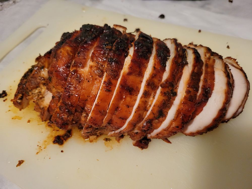 A maple-roasted turkey breast is sliced on a cutting board. It is amber red in color with a seasoned crust.