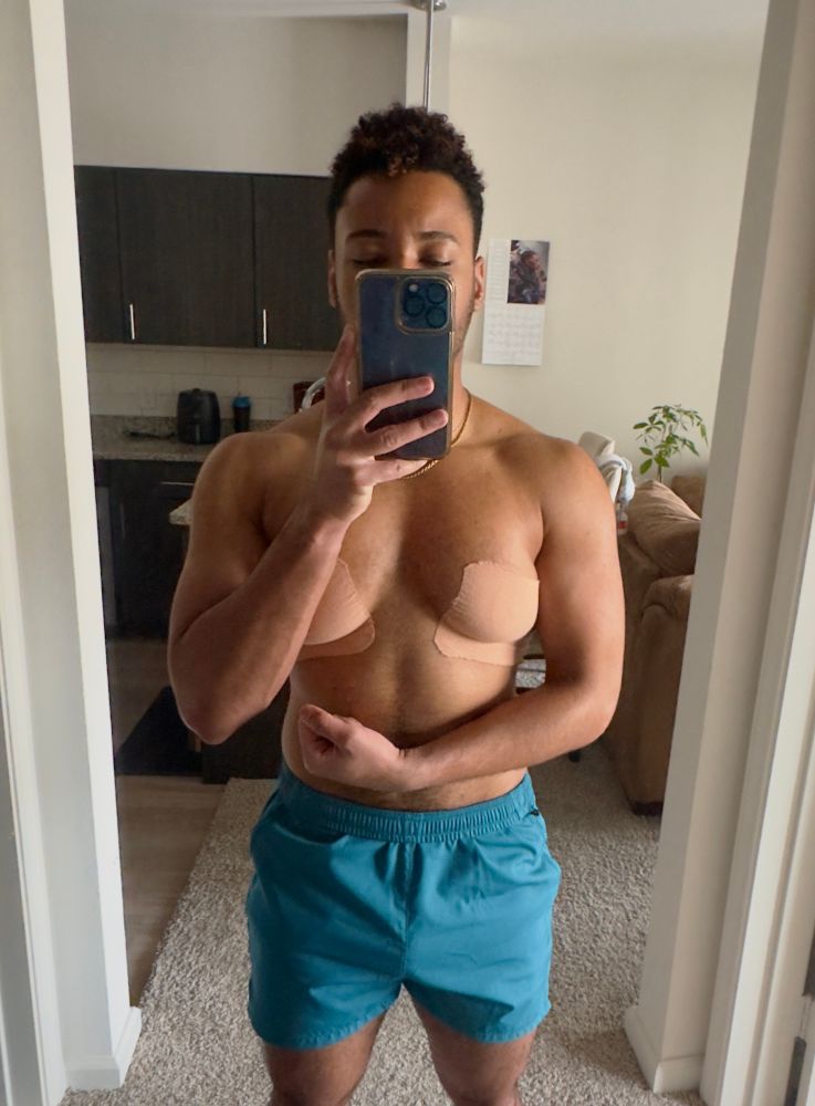 the hottest guy you know flexing chest and arms in the mirror, shirtless in short blue shorts