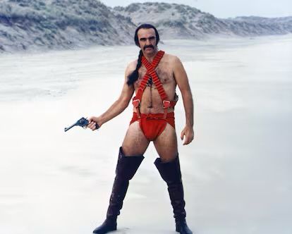 Image iconique de Sean Connery dans Zardoz portant un body-string rouge et des bottes cuissardes en brandissant un revolver. 