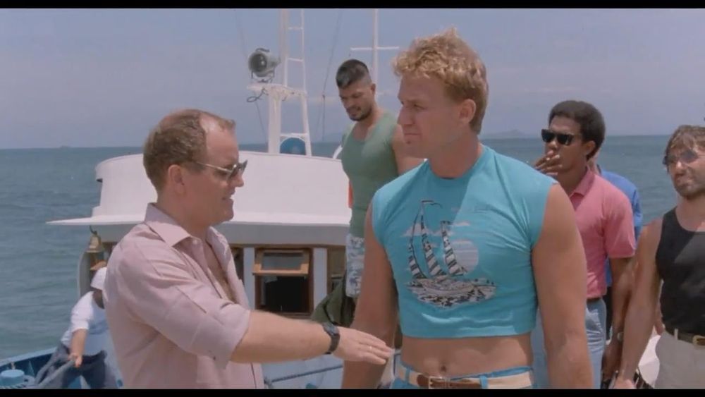 Image de Rebowar avec Reb Brown portant un t-shirt bleu électrique très moulant qui laisse voir son nombril. 