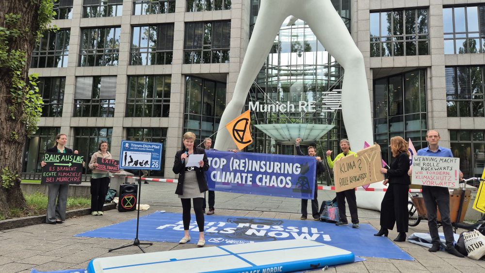 Aktivisti vor der Zentrale der Munich RE in München bei ihrer Kundgebung. 2 Aktivisti halten ein Banner "Stop (re)insuring climate chaos"