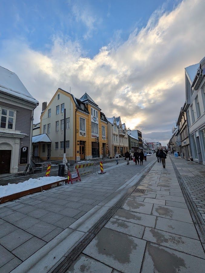 A photo of a large sidewalk with rows of buildings on either side and lots of clouds in the sky