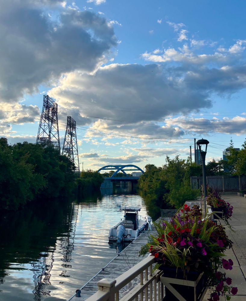 Chicago River North Branch. A boat sits along the dock. Halsted Bridge crosses the river. Power lines are strung overhead.