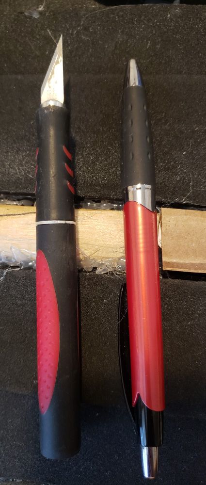 A side-by-side comparison of an exacto blade with a handle that looks very similar to a ballpoint pen. They have the same red, black, and silver colors but in slightly differing patterns.