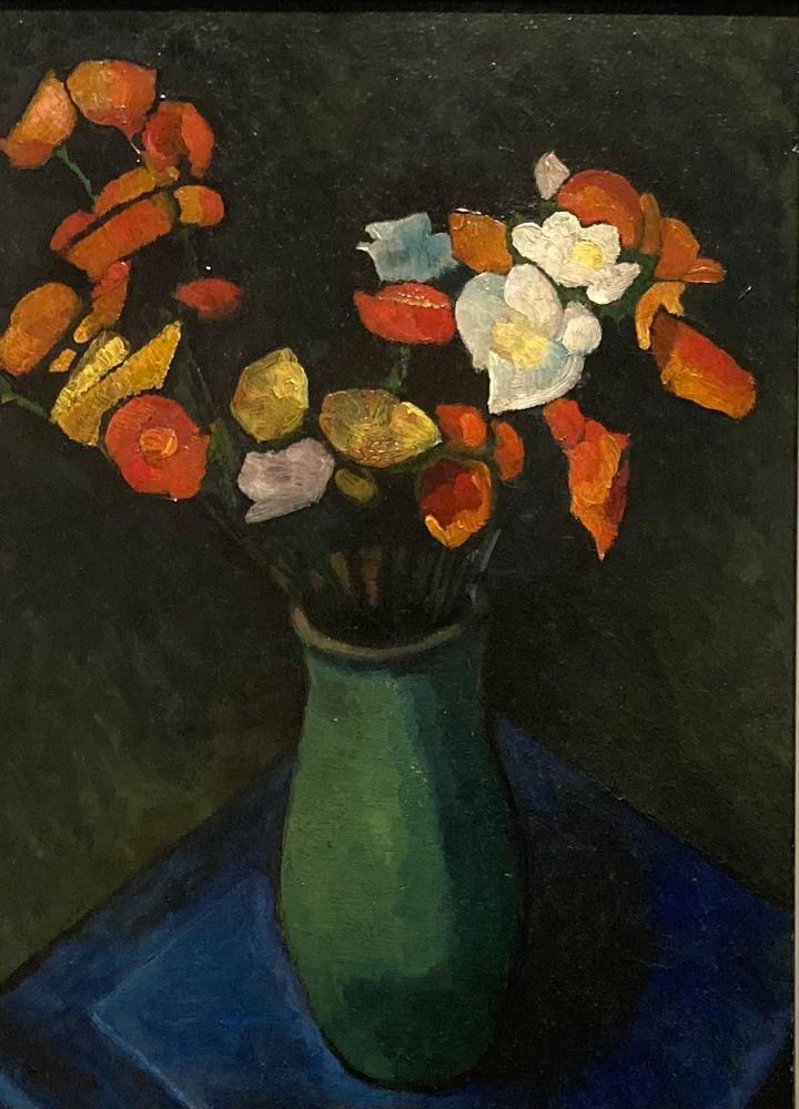 Stillleben Blumenbilder: auf einem blauen Stoff eine grüne Vase mit gelben, weißen, meist orange farbigen Blumen. Der Hintergrund ist dunkel.