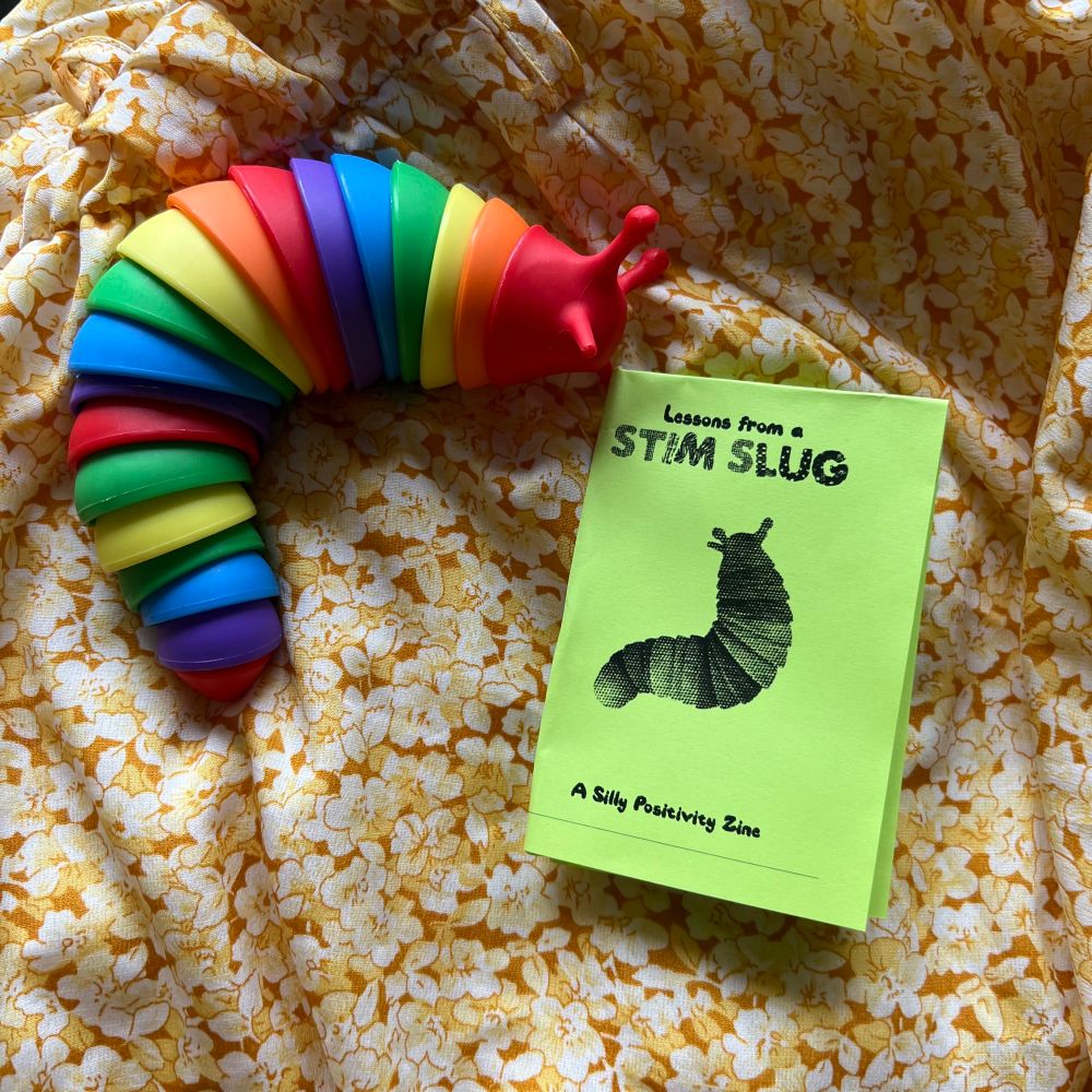 A fidget slug next to a spring green zine that has a halftone image of said slug. The title is "Lessons from a STIM SLUG: a silly positivity zine"