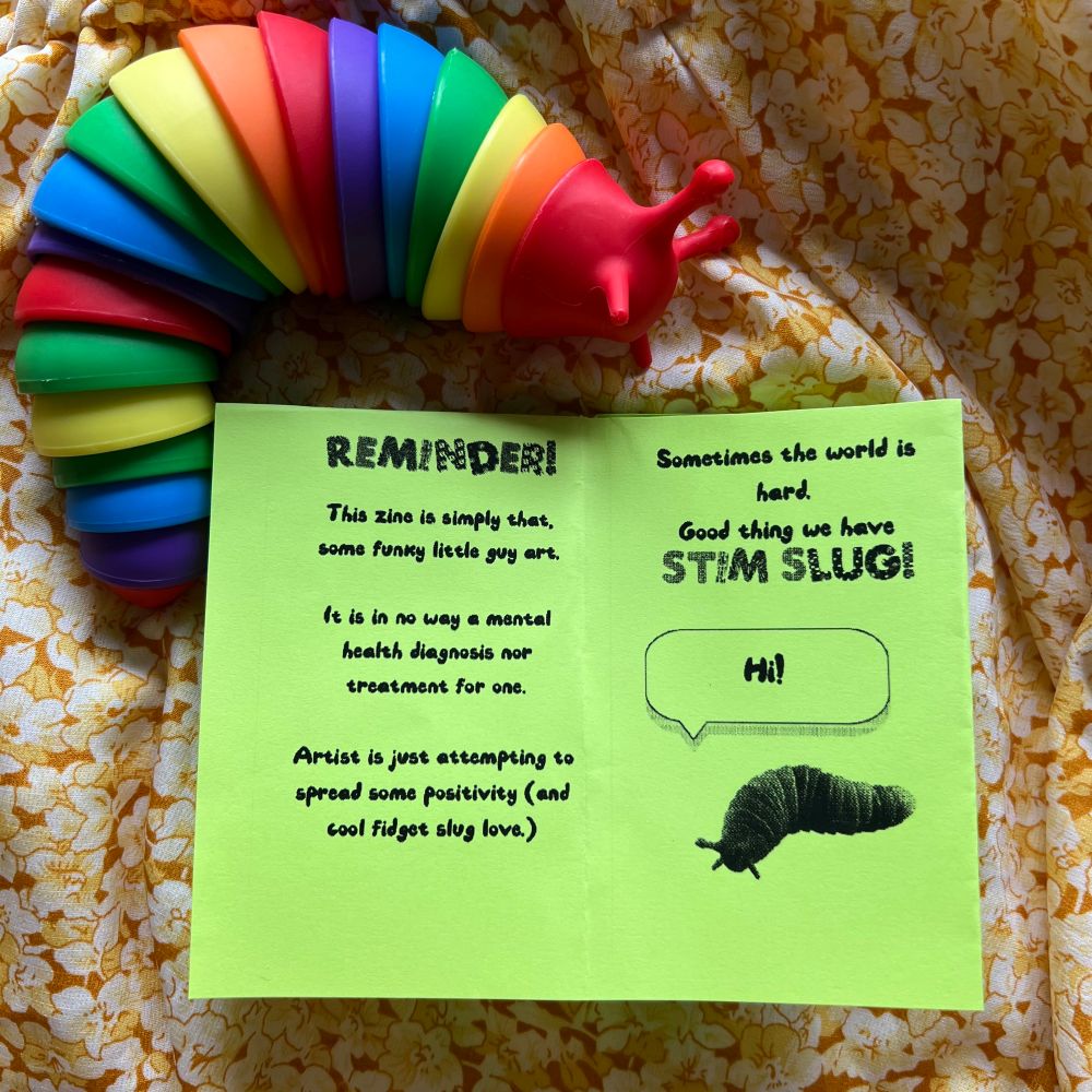 A Stim slug next to the open spring green zine. The pages read "reminder! This zine is simply that, some funny little guy art. It is in no way a mental health diagnosis nor treatment for one. Artist is just attempting to spread some positivity (and cool fidget slug love."
Next page reads "sometimes the world is hard. Good thing we have Stim slug!" The Stim slug image has a speech bubble. It is saying hi!