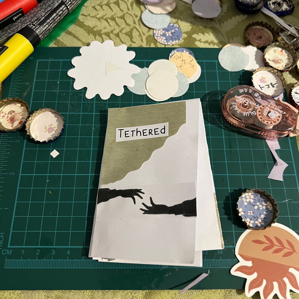 A zine on a messy craft desk. It's titled "Tethered"