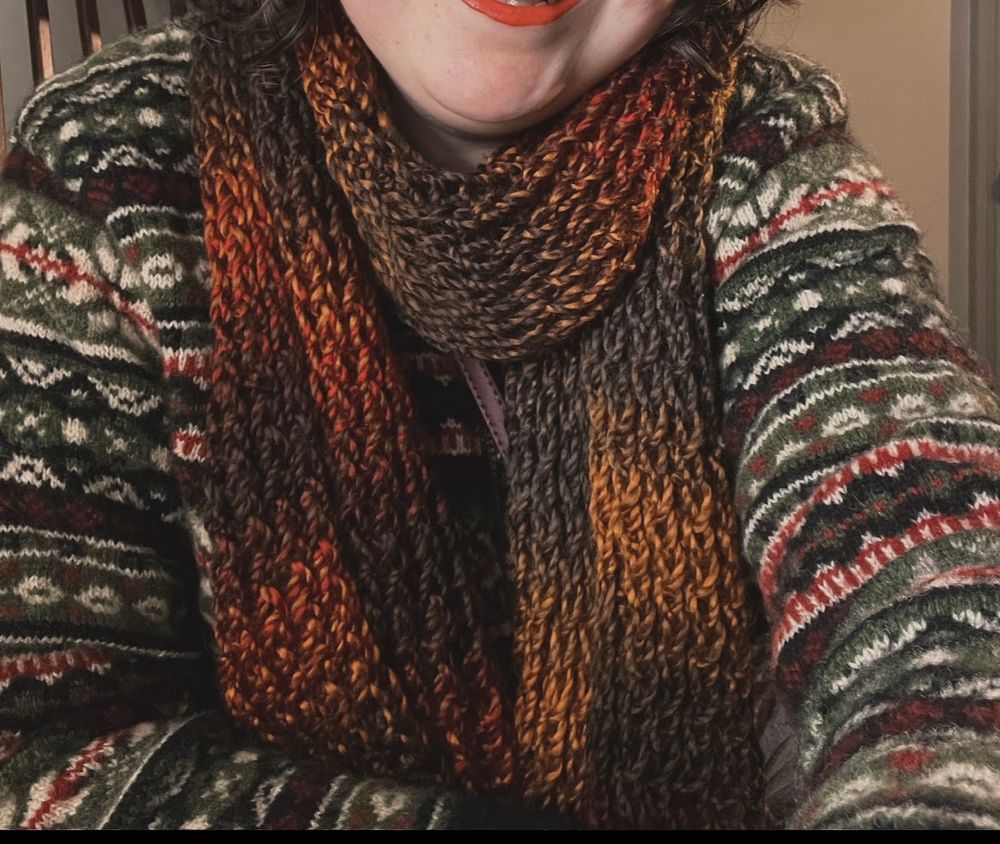 A loom knit acrylic scarf in gradient deep reds, yellows, and greens.