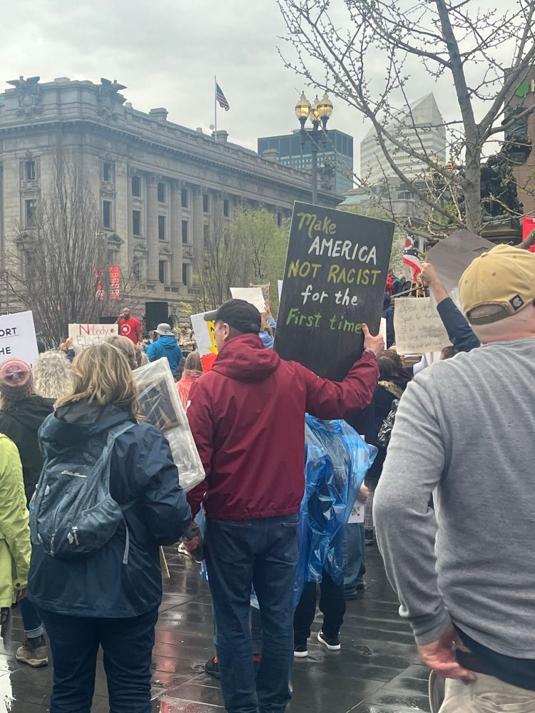 In the crowd a man holding a sign that reads “Make America not racist again”