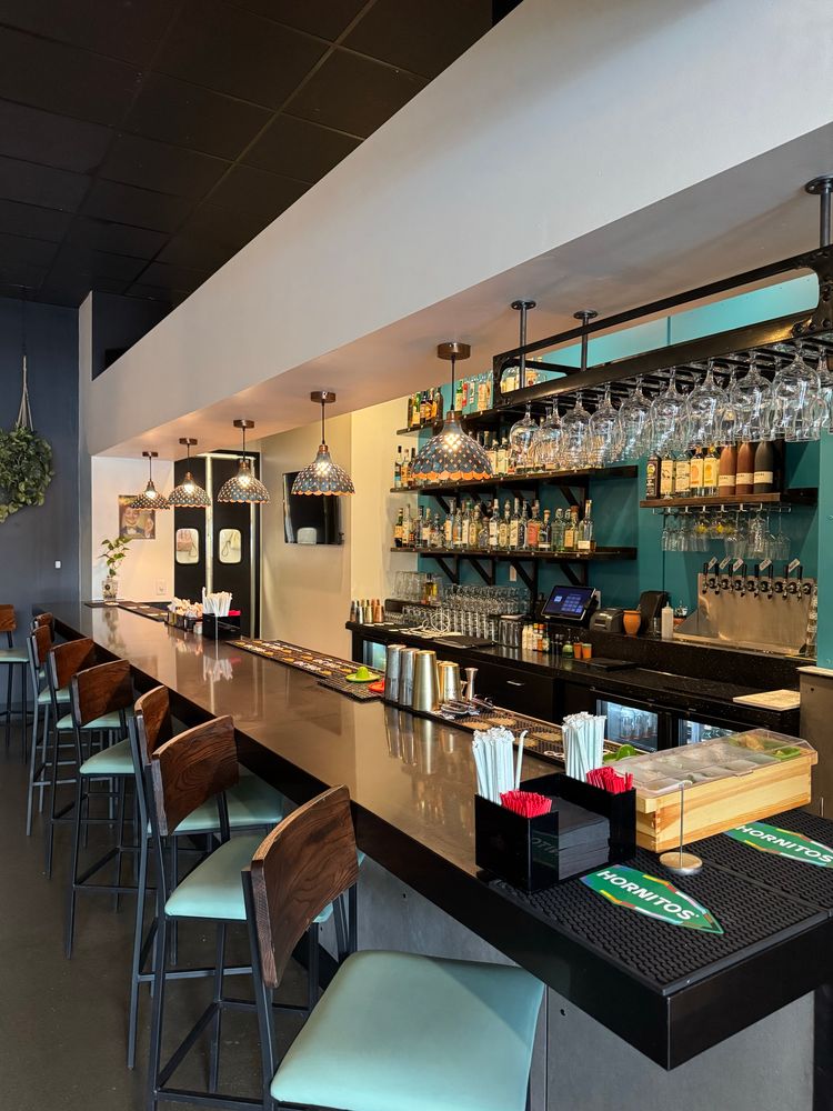 A bar top with multiple tequilas and glasses and high top seating 