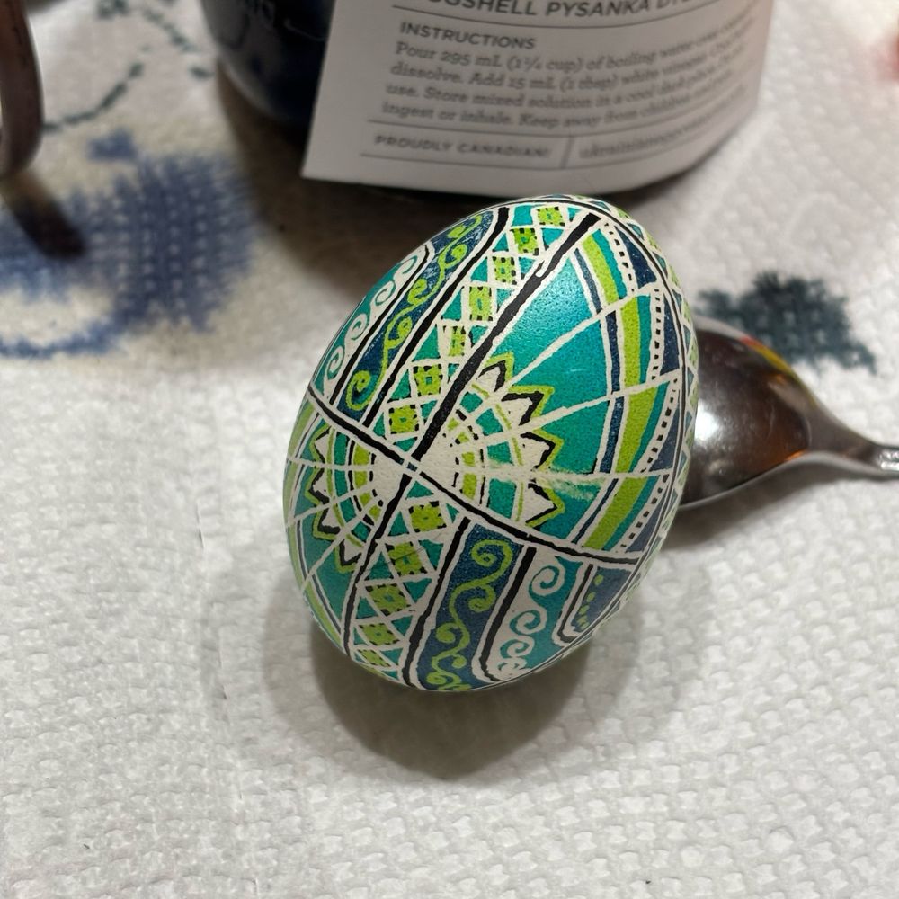 A psyanky, a traditionally dyed Ukrainian Easter egg, with intricate geometric patterns colored in blue green and teal.