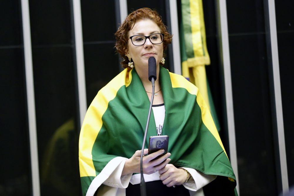 Foto da Carla Zambelli enrolada na bandeira do Brasil, no púlpito da Câmara 