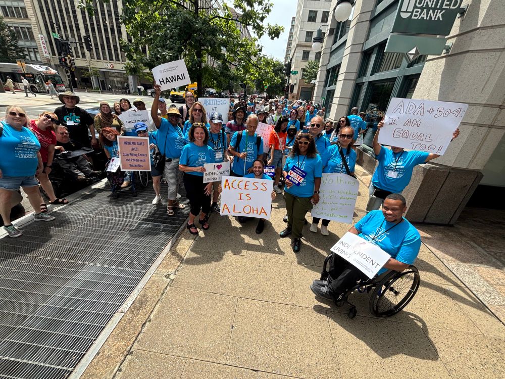 A crowd of disability rights advocates marching toward the Capitol, wearing blue shirts that celebrate the ADA’s 35th anniversary. Everyone has signs that vary from “I heart independent living,” “access is aloha,” “ADA + 504: I am equal too!” And more.