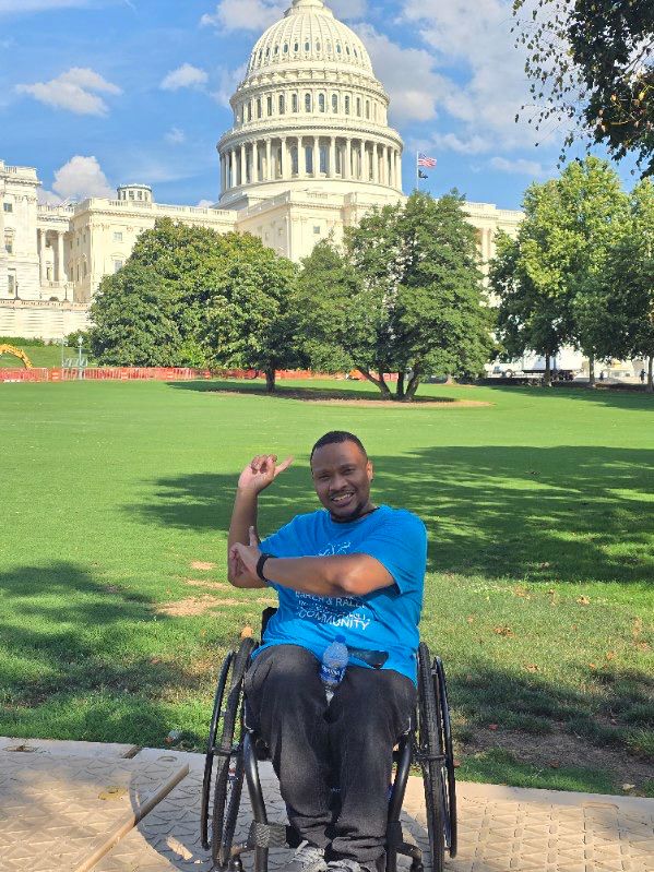 Our team member Eddie, in a wheelchair, flashing a proud smile and pointing back toward the Capitol. A symbol of how far we’ve come and how much further we’re ready to go.