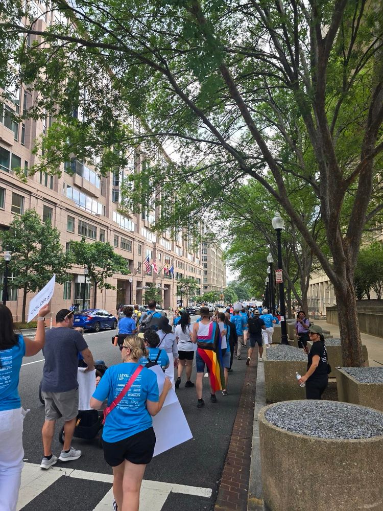 More of the crowd of support are marching towards the capitol building. All wearing blue 35th anniversary ADA shirts and marching down the street.