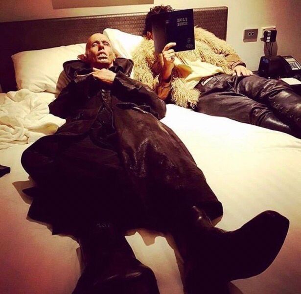personagem petyr do filme what we do in the shadows dormindo em uma cama de casal ao lado de um homem que segura uma bíblia 