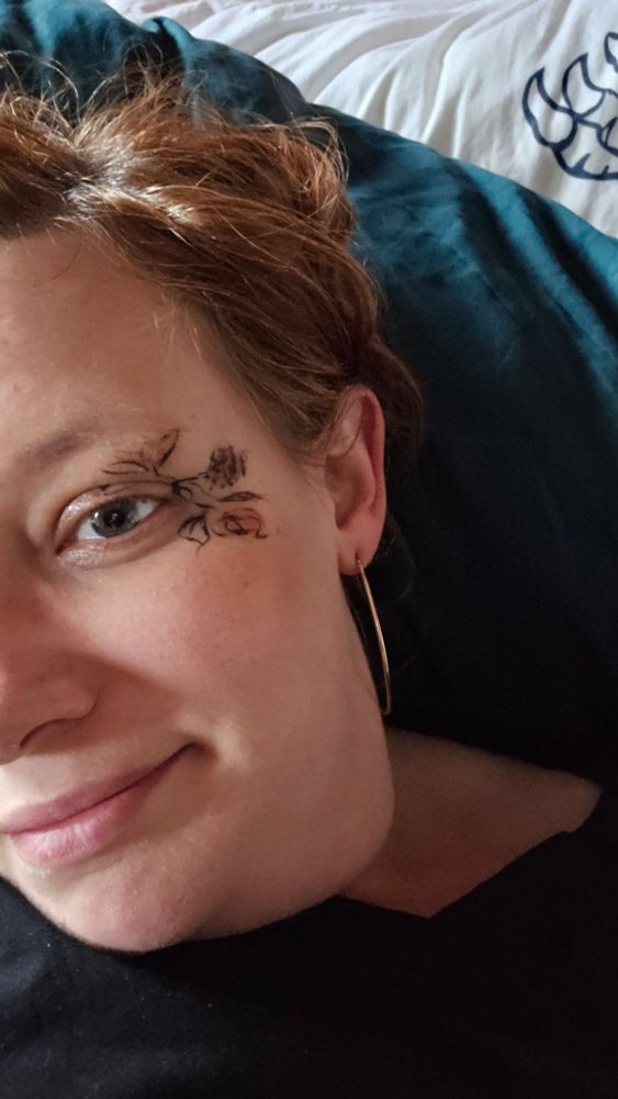 Selfie, auf dem ich halb drauf bin mit goldenem Ohrring und gemalten Blumen und Blätter am Auge. Im Hintergrund ein Kissen mit Krallenaufdruck.