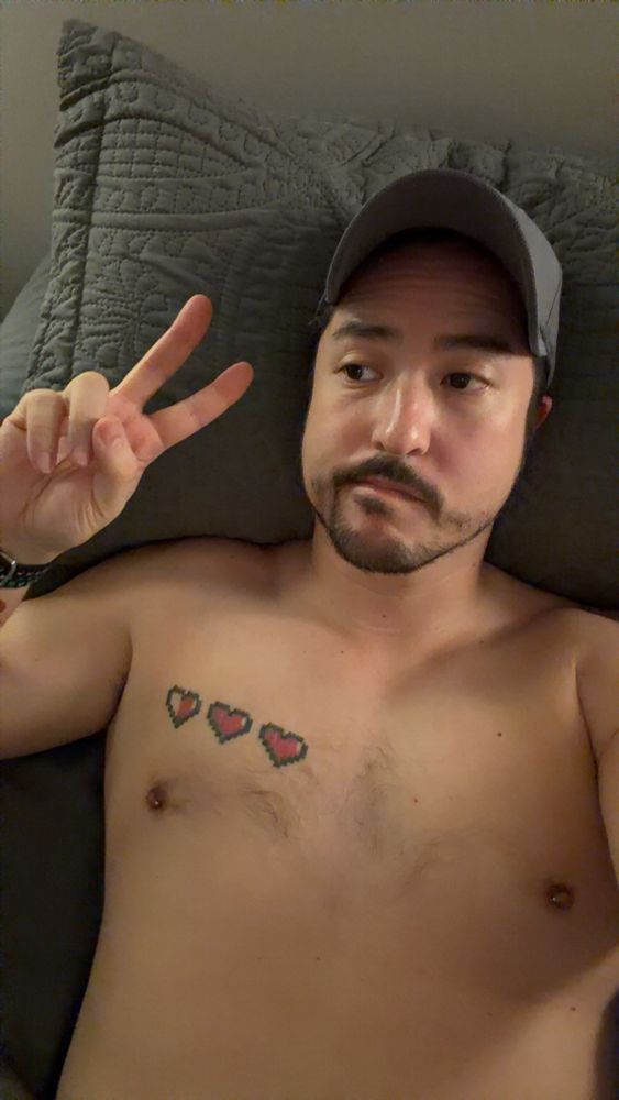 Shirtless selfie lying in bed giving the peace sign with a dejected expression upon my face 