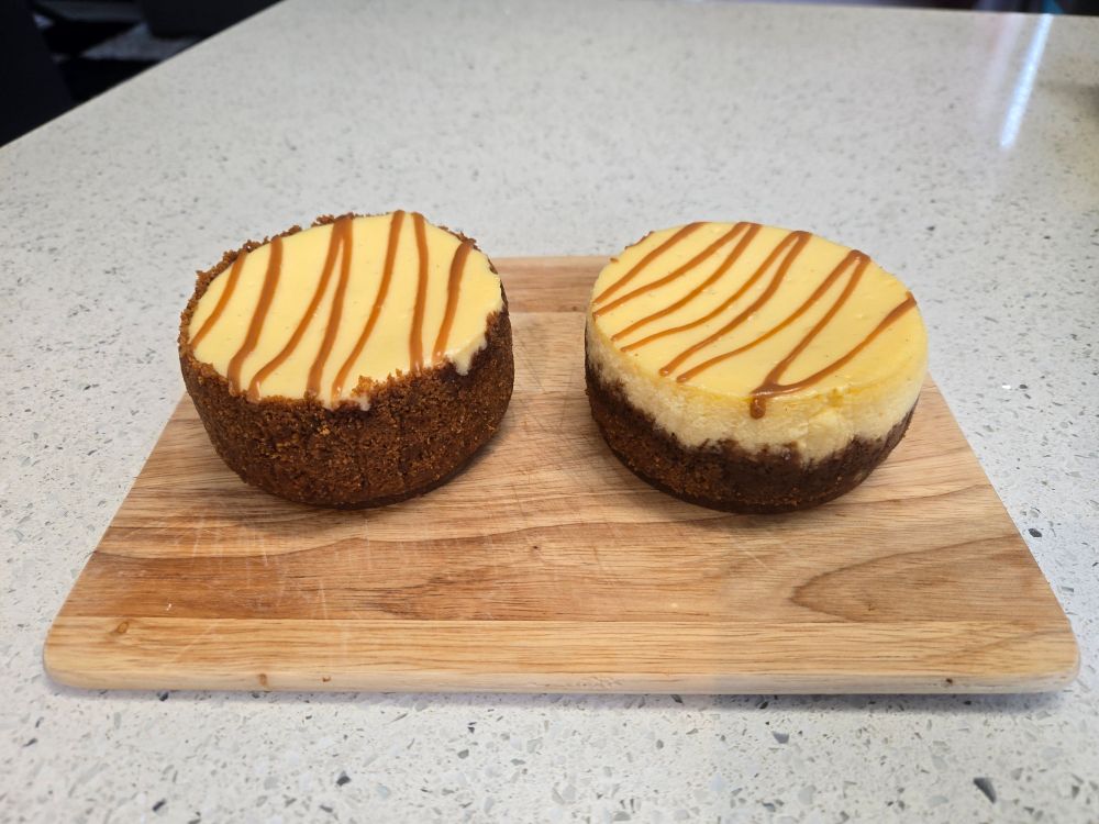 2 cheesecakes (white chocolate with a biscoff base and drizzle) sitting on a wooden board on a white benchtop